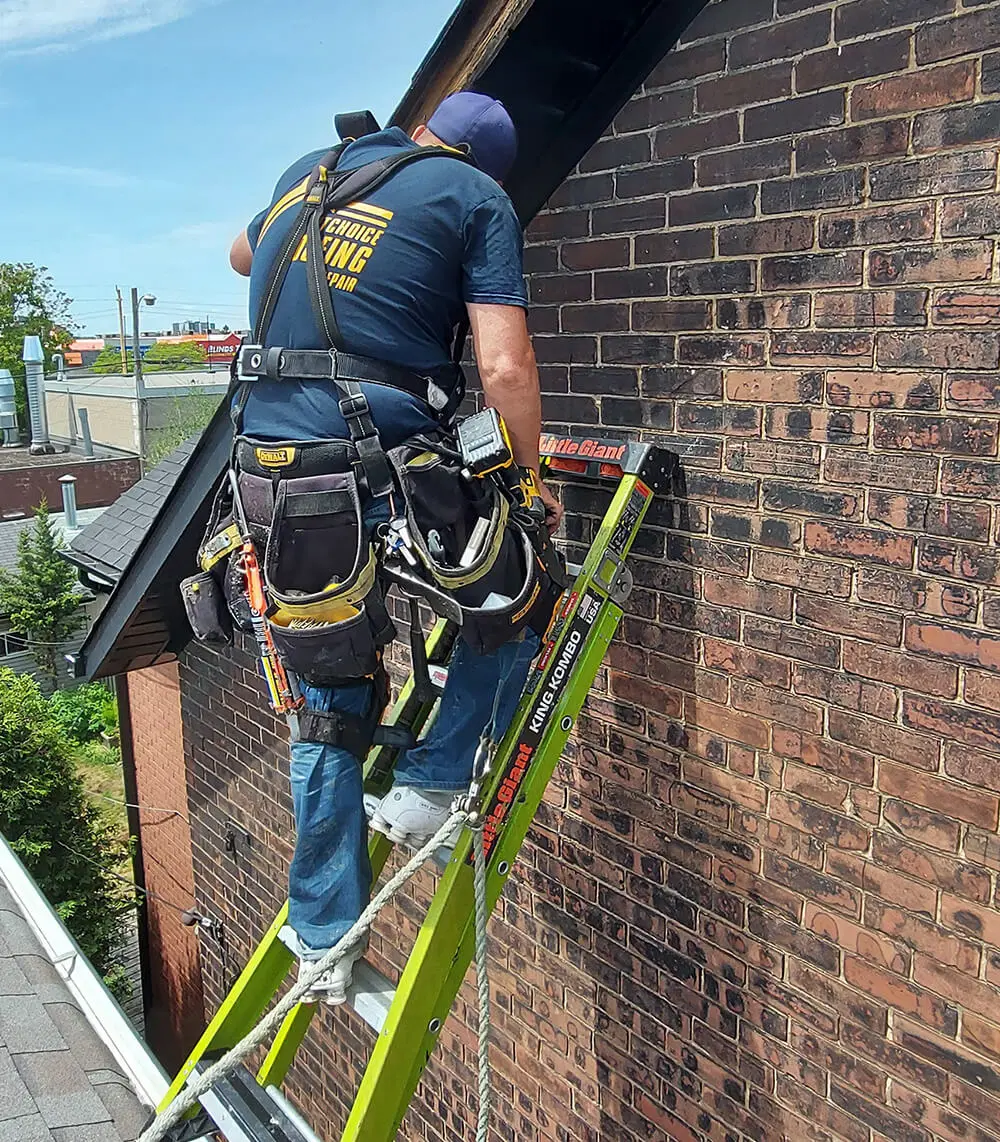 Picture of a exceptional Toronto Roofer who works for Right choice roofing and repair in a navy blue shirt and cap with company logo across the back on a step ladder that's sitting on a 3 story sloped Roof in the west end of Toronto hanging in a Rope and harness providing Wind damaged Roof Flashing repair for a very happy customer who found Right choice roofing and repair on Google and saw that they had many good reviews from many satisfied clients who chose them for Roof repair, Roof replacement and Slate Roofing services in the GTA since 2007.