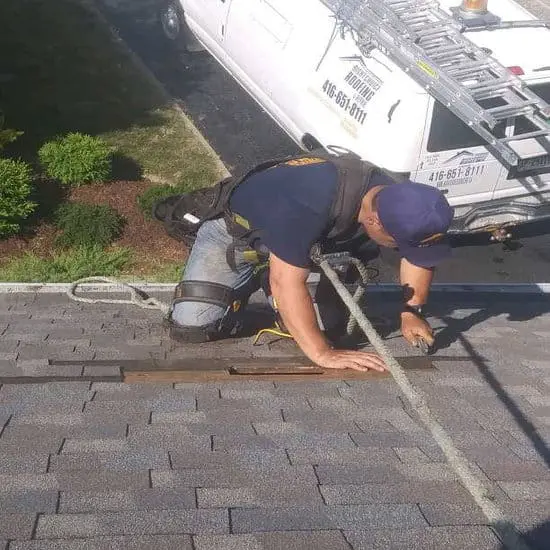 Rope-secured Toronto roofer in Right Choice Roofing and Repair gear fixes wind-damage on a steep shingle roof.