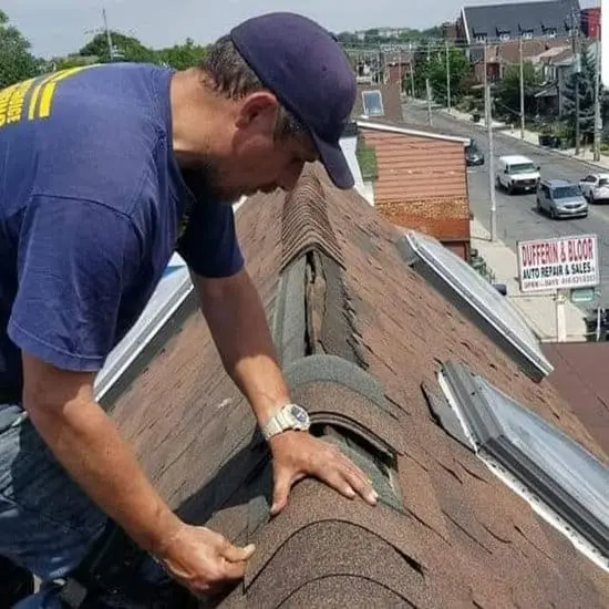 Roofer reseats ridge cap shingles on a sloped shingle roof in Toronto beside skylights&mdash;roof repair and roof replacement, with slate roofing expertise by Right Choice Roofing and Repair.