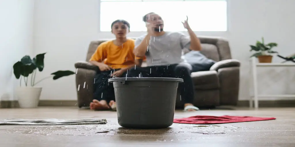 Toronto family dealing with an emergency roof leak, using a bucket to catch water while waiting for roof repair.