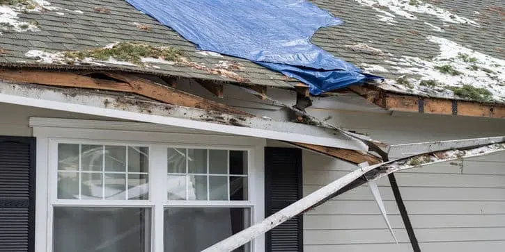 Storm-damaged Toronto shingle roof covered with a blue tarp after an ice dam roof leak, showing emergency winter roof repair.