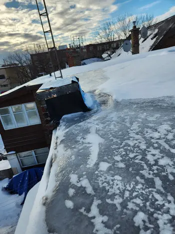 Massive ice buildup blocking flat roof drain in Toronto causing several feet of ice backup across roof surface