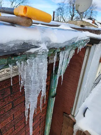 Large icicles hanging from gutters and eaves in Toronto indicating ice dam problems requiring roof repair