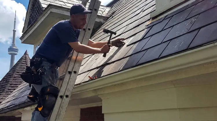 Right Choice Roofing and Repair specialist on ladder completing slate roof replacement on Toronto heritage home with natural slate tiles and CN Tower clearly visible in background