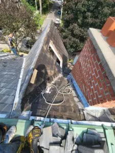Progress photo showing 100 year old slate tiles being stripped from main roof slope next to brick chimney during full replacement project in Harbord Village Toronto by Right Choice Roofing and Repair