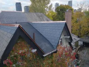 Close aerial view of a completed natural Slate Roof and flat Roof replacement on a Rosedale Toronto heritage home with new copper Ridge and Hip Flashing, Toronto skyline in background