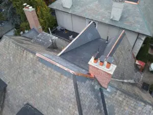 Aerial view of replaced natural Slate Roof tiles and flat Roof section in Rosedale Toronto with new copper Counter Flashing around the brick Chimney