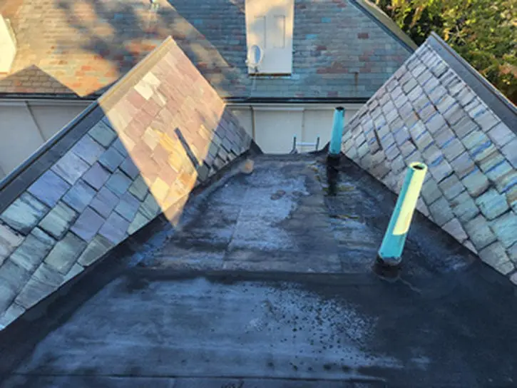 Before photo of a failing flat Roof and aging natural Slate Roof in Rosedale Toronto with mismatched patched Slates and worn vent stacks