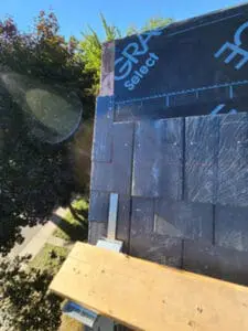 Bird's eye progress photo looking straight down from steep slate roof showing new slate tiles being installed with copper nails and wood plank work platform on metal jacks with backyard visible below in Harbord Village Toronto by Right Choice Roofing and Repair
