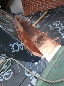 Progress photo showing custom fabricated hemmed copper valley junction flashing laid out on Grace Select underlayment alongside brick chimney during slate roof replacement in Harbord Village Toronto by Right Choice Roofing and Repair
