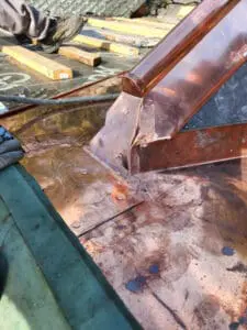 Progress photo showing custom fabricated copper piece being hand fitted to close ridge and tie into copper flat roof below during slate roof replacement in Harbord Village Toronto by Right Choice Roofing and Repair