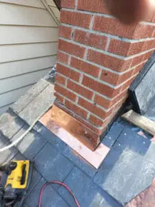 Progress photo showing custom fabricated copper front pan chimney flashing fully installed at brick chimney corner with new slate tiles fitted tight on both sides during slate roof replacement in Harbord Village Toronto by Right Choice Roofing and Repair