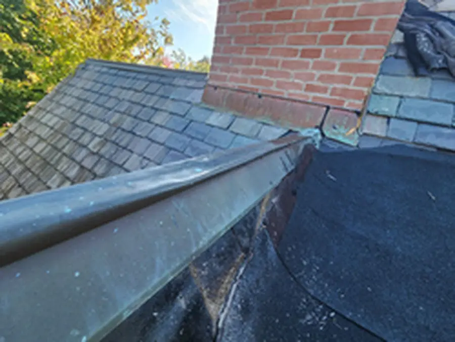 Tear-off in progress at the brick Chimney showing old copper Ridge Cap and weathered Slate tiles on a Rosedale Toronto Roof replacement