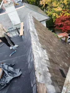 Frank removing Slate tiles from the opposite side of a Dormer sloped Roof in Rosedale Toronto after lifting the Ridge Cap Flashing to replace both systems properly