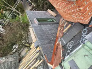 Progress photo from flat roof showing new slate tiles partially installed on main slope with Velux skylight wood plank work platforms on metal jacks and 2x4 step ups during slate roof replacement in Harbord Village Toronto by Right Choice Roofing and Repair