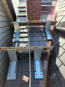 Progress photo showing multiple work platforms set up using slate roof jacks and wood planks around brick chimney on steep slate roof during slate roof replacement in Harbord Village Toronto by Right Choice Roofing and Repair