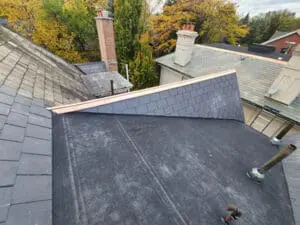 Final wide view of a completed heritage Slate Roof and flat Roof replacement on a Rosedale Toronto home with new modified bitumen flat Roof, new natural Slate on the Dormer, copper Hip Cap, and brick Chimneys by Right Choice Roofing and Repair