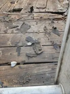 Close-up of rotted wood board decking with old tar debris and Slate fragments exposed during a flat Roof leak repair in Rosedale Toronto