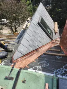 Progress photo showing heritage building dormer with new slate tiles mostly installed copper drip edge and Velux skylight fitted during slate roofing services in Harbord Village Toronto by Right Choice Roofing and Repair