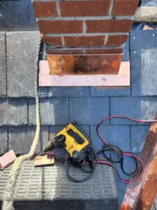 Progress photo showing custom fabricated copper front pan chimney flashing being installed at base of brick chimney with new slate tiles surrounding it and DeWalt drill staged during slate roof replacement on heritage home in Harbord Village Toronto by Right Choice Roofing and Repair