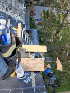 Progress photo looking straight down from steep slate roof showing local Toronto slate roofer boots tool belt and wood plank work platform on metal jacks with backyard visible below in Harbord Village Toronto by Right Choice Roofing and Repair