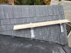 Slate tile installation in progress on one side of a Dormer sloped Roof on a Rosedale Toronto heritage home with a work platform of jacks and plank set up for safe access