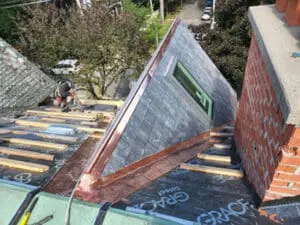 Progress photo from flat roof showing full dormer nearly complete with new slate tiles copper valley copper drip edge and Velux skylight fitted alongside brick chimney during precise slate roof installation in Harbord Village Toronto by Right Choice Roofing and Repair