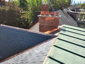 Final photo showing precision slate roof replacement by Right Choice Roofing and Repair with completed new slate tiles copper drip edge copper flat roof and brick chimney with clay flues against Harbord Village Toronto neighbourhood backdrop