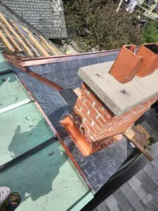 Progress photo from flat roof showing completed copper chimney flashing kit on all four faces of brick chimney with new slate tiles on main slope and copper flat roof section in foreground during slate roof replacement in Harbord Village Toronto by Right Choice Roofing and Repair