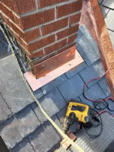 Progress photo showing copper front pan chimney flashing being rivet fastened into mortar joint at base of brick chimney with new slate tiles and DeWalt drill staged during slate roof replacement in Harbord Village Toronto by Right Choice Roofing and Repair
