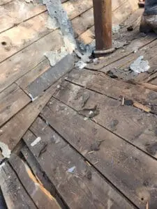 Rotted wood Roof boards around an old cast-iron vent pipe exposed during flat Roof tear-off in Rosedale Toronto with split Sheathing and debris