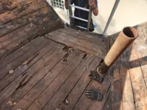 Severely water-damaged wood board substrate exposed during flat Roof tear-off in Rosedale Toronto with staining and rot around old cast-iron vent pipe