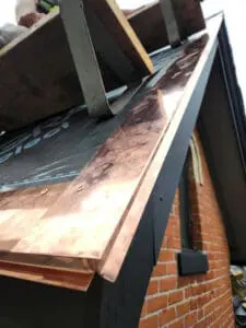 Progress photo showing copper drip edge being hand bent and fitted on site at gable edge alongside brick chimney during slate roof replacement in Harbord Village Toronto by Right Choice Roofing and Repair