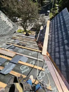Progress photo looking down main slope showing new slate tiles installed on one section with Grace Select exposed on other section wood plank work platform on metal jacks 2x4 step ups and rope safety line during slate roof replacement staging in Harbord Village Toronto by Right Choice Roofing and Repair
