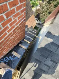 Progress photo showing Grace ice and water shield waterproofing layer being installed along eave line with new copper drip edge at base of brick chimney during slate roof replacement in Harbord Village Toronto by Right Choice Roofing and Repair