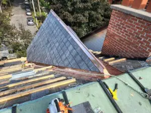 Progress photo from flat roof showing dormer with slate tiles installed and copper ridge cap closures being fitted at peak with copper valley and brick chimney visible during slate roof replacement in Harbord Village Toronto by Right Choice Roofing and Repair