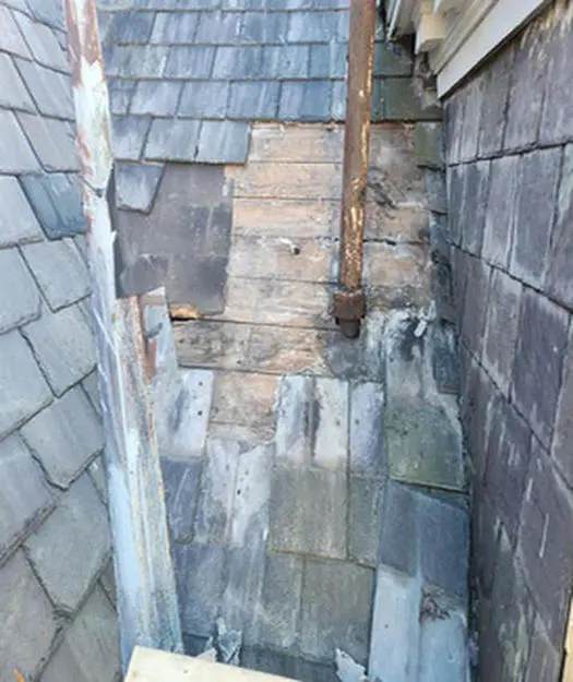 Slate tiles removed exposing rotted roof decking around a failed plumbing exhaust pipe on a Toronto heritage home
