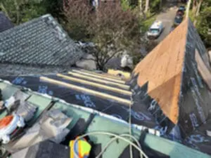 Progress photo taken from steep main slope looking down toward street showing new plywood sheathing with 2x4 step ups and tools staged on flat roof below during slate roof replacement in Harbord Village Toronto by Right Choice Roofing and Repair