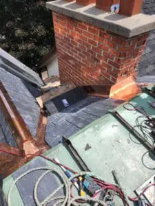 Progress photo showing completed copper chimney flashing kit fully installed on all faces of brick chimney with new slate tiles surrounding it and copper flat roof section below during slate roof replacement in Harbord Village Toronto by Right Choice Roofing and Repair